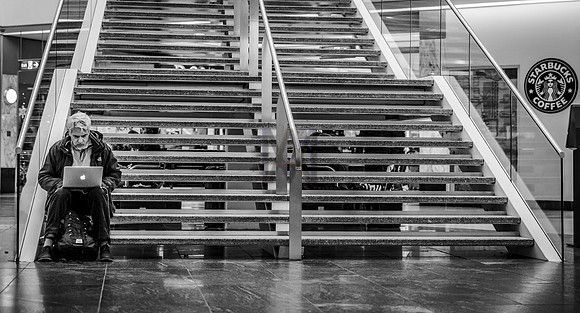 A man sits on the steps of a shopping mall using his laptop. Image made by Preston based street photographer Alf Myers